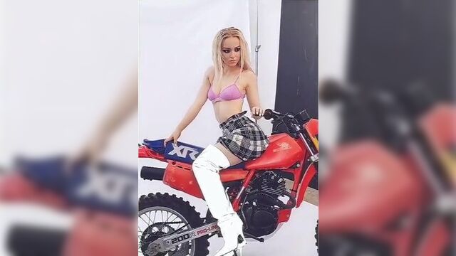 Dove Cameron in a pink bra straddling a motorcycle